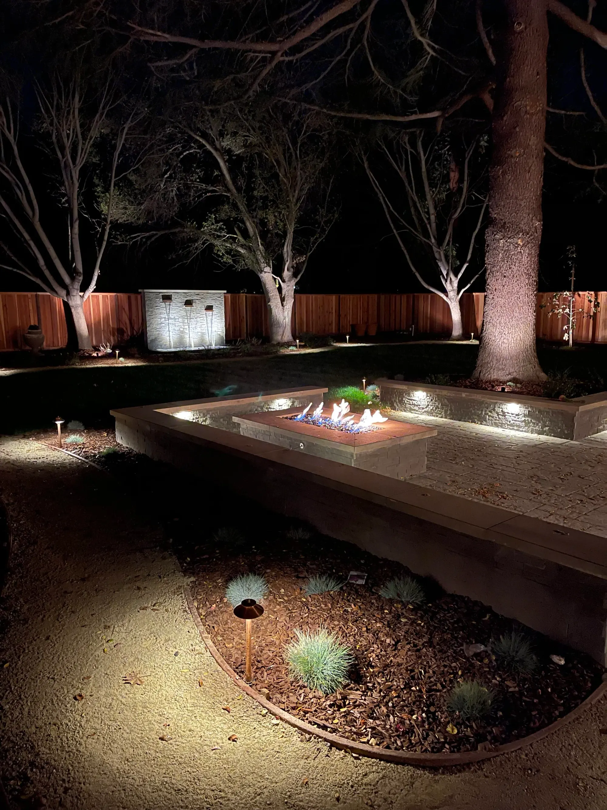 Fire table in a gravel garden with uplit trees at night
