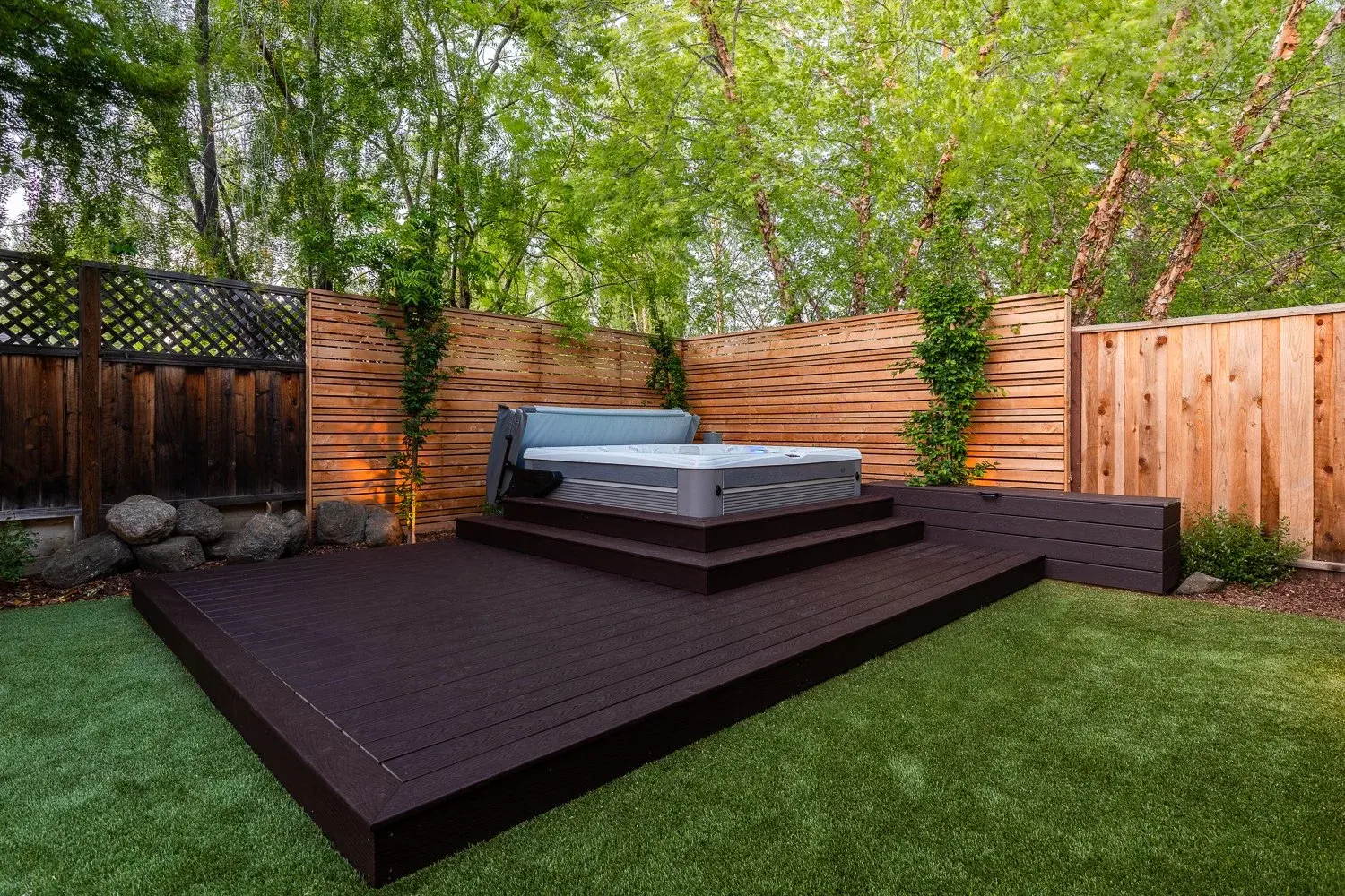 Hot tub set on a dark wood deck against a cedar fence