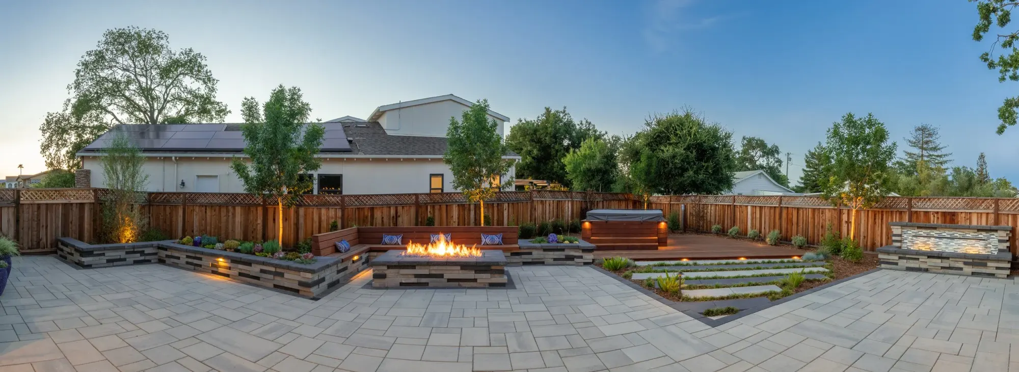 Panorama of a paver backyard with a fire pit and planting beds